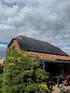 Schwarze Solarpaneele auf einem Ziegeldach über einer Terrasse mit Gartenmöbeln und üppigem Grün.