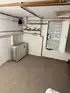 Ein sauberer Kellerraum mit einem weißen Energie-/Batteriespeicher, Kupferrohren und einem offenen Sicherungskasten an der Wand.