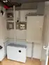 Weißer Energiespeicher von "bigenergy" mit grün leuchtender Anzeige steht auf braunen Fliesen unter Schaltschränken.